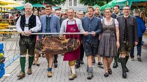 Wie eine Trophäe wird die ganze Speckseite von Produzent Markus Schluder (Mitte) und den Ehrengästen durch die Menge zum Anschnitt auf den Hauptplatz getragen 