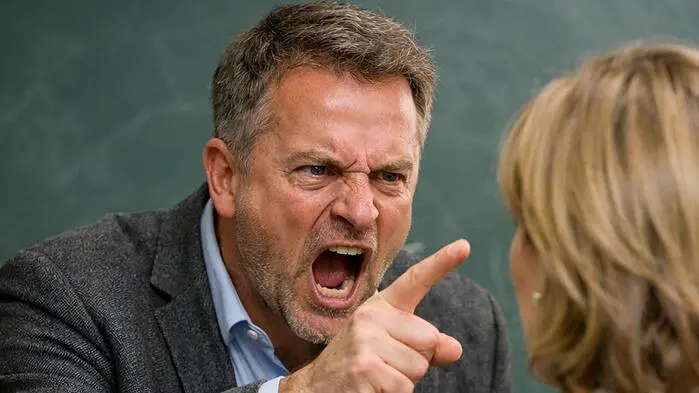 Ein Lehrer schreit mit erhobenem Zeigefinger eine Frau an | Respektlos und unprofessionell soll der Umgangston des Schulleiters sein (Symbolbild)