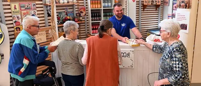 Vier ältere Menschen stehen an einer Verkaufstheke, wo ein Pfleger verschiedene Produkte ausgibt.