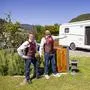 Zwei Männer mittleren Alters stehen in traditionellem Gewand vor einem Campingwagen