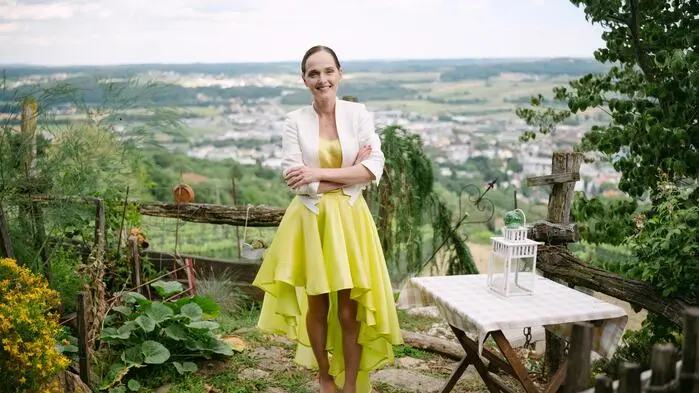 Eine Frau in einem gelben Kleid steht neben einem Gartentisch.