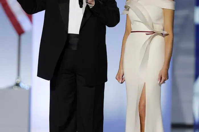Beim Inauguration Ball 2017 wählte First Lady Melania Trump ein schulterfreies Kleid aus vanillefarbenem Seidenkrepp des Designers Hervé Pierre. Um die Taille war ein weinrotes Band geschnürt.  