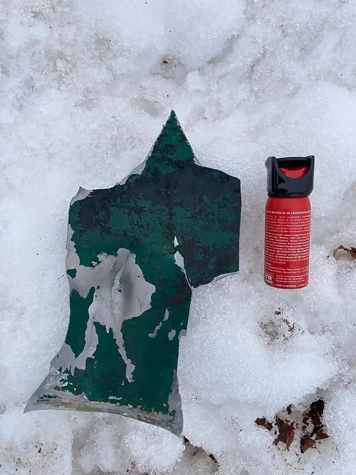 Weggeschleudertes Stahlblech-Fragment des zerstörten Mülleimers in Velden.  Die Pfefferspray-Dose dient als Größenvergleich