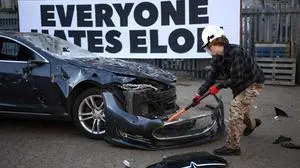 A person smashes a Tesla car during anti Elon Musk protest at Hardess Studios in south London on April 10, 2025. (Photo by HENRY NICHOLLS / AFP)