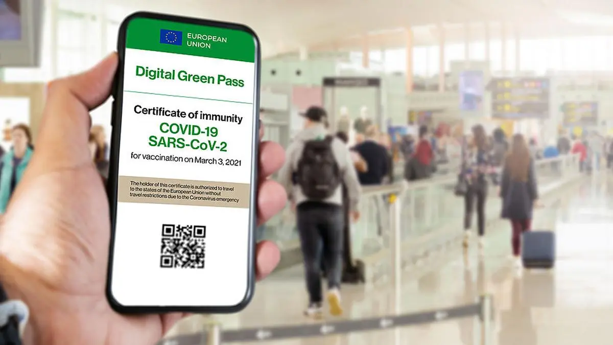 The digital green pass of the european union with the QR code on the screen of a mobile held by a hand with blurred airport in the background. Immunity from Covid-19. Travel without restrictions.
