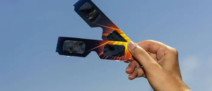 Das Bild zeigt eine Hand, die zwei Sonnenfinsternisbrillen in die Luft hält