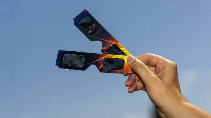 Das Bild zeigt eine Hand, die zwei Sonnenfinsternisbrillen in die Luft hält