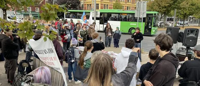 Eine Gruppe Demonstrierender steht mit Transparenten vor einem Redner