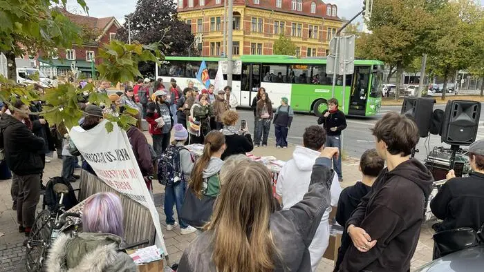 Eine Gruppe Demonstrierender steht mit Transparenten vor einem Redner