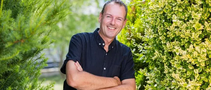 Ein Mann mit verschränkten Armen steht zwischen zwei Sträuchern