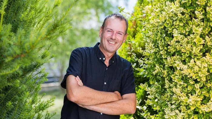 Ein Mann mit verschränkten Armen steht zwischen zwei Sträuchern