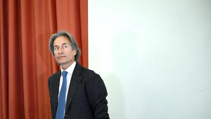 Ex-Finanzminister Karl-Heinz Grasser vor einem roten Vorhang und einer weißen Wand.