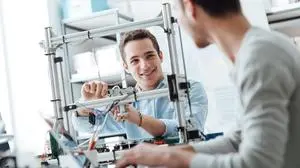 Engineering students working in the lab, a student is adjusting a 3D printer's components, the other one on foreground is using a laptop