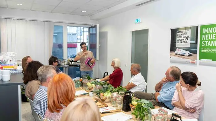 Eine Gruppe von Menschen sitzt an einem langen Tisch voll mit Gemüse und Zubehör zum Fermentieren