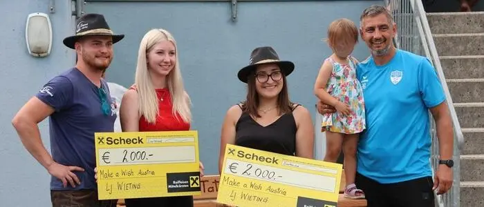 Zwei Frauen und zwei Männer lächeln in die Kamera. Die zwei Frauen halten einen Scheck in den Händen, der Mann rechts hält ein Kind auf dem Arm.