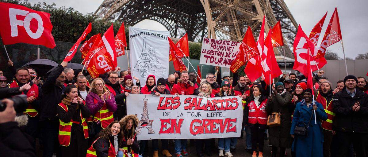 Streikende mit Transparenten vor dem Eiffelturm in Paris.  | Die Gewerkschaften der Eiffelturm-Betreiberfirmen warnen mit einem Streik vor einer für aus ihrer Sicht gefährlichen Misswirtschaft. Tatsächlich nagt der Rost am Pariser Wahrzeichen. 