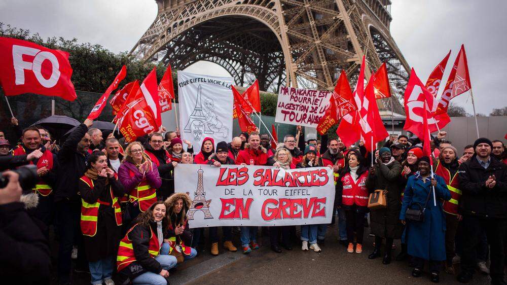 Streikende mit Transparenten vor dem Eiffelturm in Paris.  | Die Gewerkschaften der Eiffelturm-Betreiberfirmen warnen mit einem Streik vor einer für aus ihrer Sicht gefährlichen Misswirtschaft. Tatsächlich nagt der Rost am Pariser Wahrzeichen. 