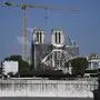 A man carries a suitcase as he walks across a bridge and looks at Notre-Dame de Paris cathedral, on April 14, 2021, during the reconstruction work while April 15, 2021 will mark the two years anniversary of the fire that devastated the Cathedral, in the centre of the French capital Paris. (Photo by Anne-Christine POUJOULAT / AFP)