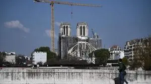 A man carries a suitcase as he walks across a bridge and looks at Notre-Dame de Paris cathedral, on April 14, 2021, during the reconstruction work while April 15, 2021 will mark the two years anniversary of the fire that devastated the Cathedral, in the centre of the French capital Paris. (Photo by Anne-Christine POUJOULAT / AFP)
