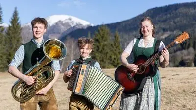 Drei junge Musiker mit Instrumenten vor einer Bergkulisse