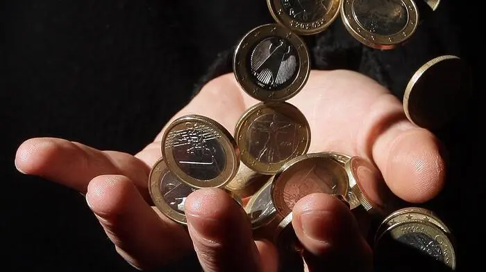 Euromünzen rieseln in eine ausgestreckte Hand