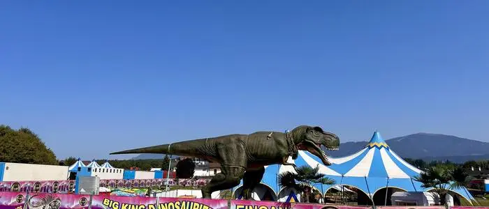 Ein großer Dinosaurier aus Plastik vor einer niedrigen Absperrung mit Werbeplakaten für die Ausstellung