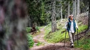 Active senior woman walking with Nordic poles while enjoying hike in beautiful autumn forest