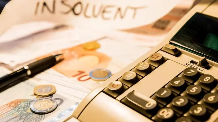 Auf dem Foto sieht man eine Rechenmaschine, ein bisschen Bargeld und eine Notiz, auf der „Insolvent“ steht