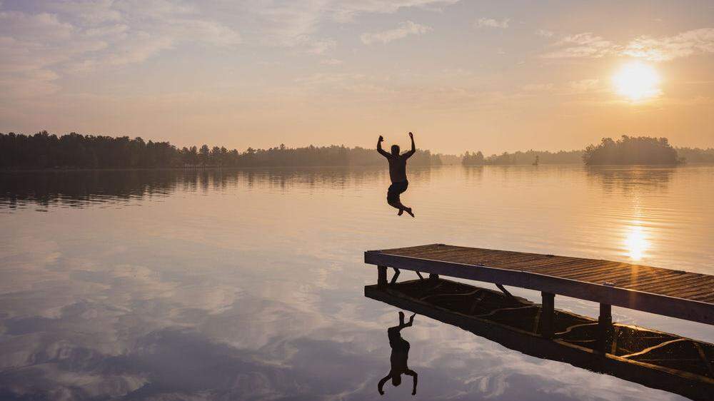 Man jumping off dock into lake at sunrise