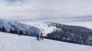 Drei Skifahrer stehen auf einer Skipiste, der Himmel ist bewölkt und überall liegt Schnee
