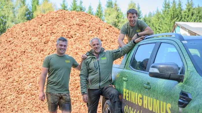 Drei Männer posieren für ein Foto und lächeln in die Kamera. Einer davon steht auf einem Pickup, die anderen beiden daneben.