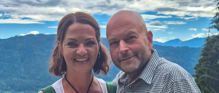 Eine Frau und ein Mann in Tracht stehen auf einer Terrasse mit weitläufigem Blick ins Tal