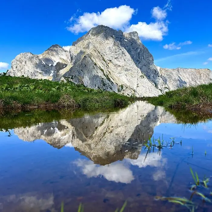 Natur in Symmetrie | Der Kaiserschild, ein markanter Gipfel in den Ennstaler Alpen, spiegelt sich im klaren Wasser des Bergsees.