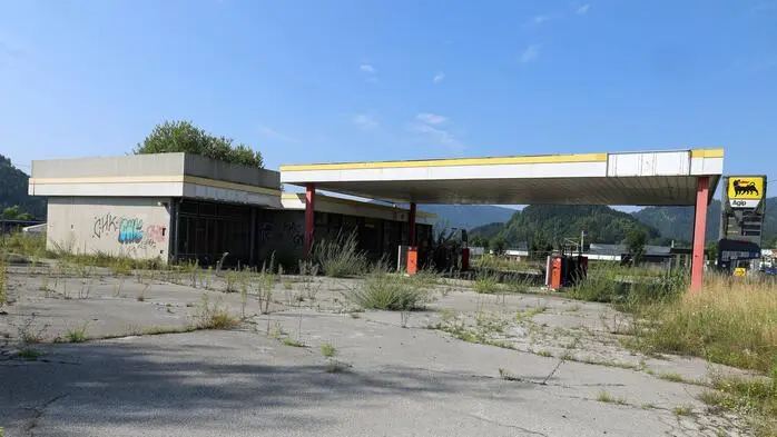 Eine veraltete und verwitterte Tankstelle. Überall wächst Unkraut, der Beton ist kaputt und Graffiti ist an der Wand.
