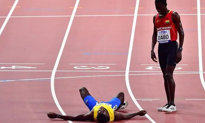 Aruba's Jonathan Busby (L) collapses after crossing the finish line in the hands of Guinea-Bissau's Braima Suncar Dabo during the Men's 5000m heats at the 2019 IAAF World Athletics Championships at the Khalifa International stadium in Doha on September 27, 2019. (Photo by Giuseppe CACACE / AFP)