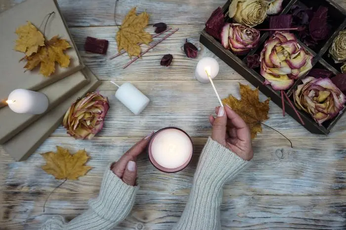 A woman lights an aromatic candle. There are dried roses in a box on the table and yellow maple leaves are lying. A woman lights an aromatic candle. There are dried roses in a box on the table and yellow maple leaves are lying. . High quality photo Copyright: x RECORD DATE NOT STATED
