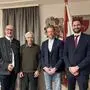 Vier Männer stehen vor einer Wand mit Wappen der Gemeinde Treffen und lächeln in die Kamera
