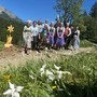11 Personen in Tracht stehen bei prächtigem Wetter vor einer hölzernen Narzisse.