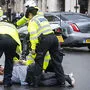 Polizisten ringen den Demonstranten nieder. Im Hintergrund der Jaguar Boris Johnsons