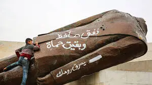 Ein Kind klettert auf eine gestürzte Statue des ehemaligen syrischen Machthabers Hafez al-Assad in der Stadt Hama