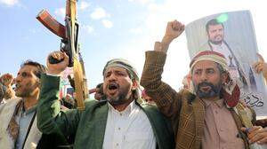 Jemenitische Männer schwingen ihre Waffen und halten Porträts des Huthi-Führers Abdul Malik al-Houthi hoch.