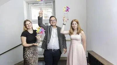 Ein Mann und zwei Frauen halten einen Pokal in die Luft