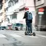 Das Foto zeigt eine Person mit einem roten Sturzhelm, die auf einem E-Scooter fährt. 