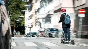 Das Foto zeigt eine Person mit einem roten Sturzhelm, die auf einem E-Scooter fährt. 