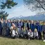 34 Frauen stehen in einer Wiese, im Hintergrund sieht man Berge 
