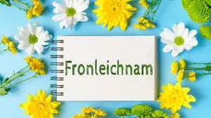 Germany - May 26, 2025: PHOTOMONTAGE, A notepad with the inscription: Corpus Christi, lies on a blue background and is framed by yellow, white and green flowers *** FOTOMONTAGE, Ein Notizblock mit der Aufschrift: Fronleichnam, liegt auf blauem Hintergrund und ist von gelben, weißen und grünen Blumen eingerahmt