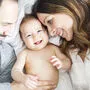 Mother father and baby child on a white bed.