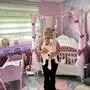 Eine blonde Frau steht inmitten eines pinken Kinderzimmers mit einem Baby an der Brust.