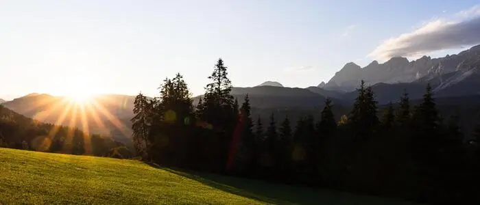 Die Sonne geht über einem Bergkamm am Horizont unter und scheint auf eine grüne Alm irgendwo in der Steiermark