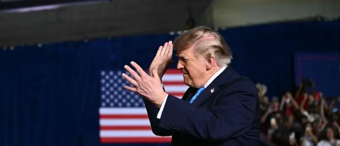 Donald Trump klatscht in die Hände. Hinter ihm ist die US-Flagge.